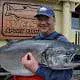 A man poses holding his Chinook salmon catch in front of King Pacific Lodge