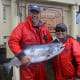 A man and a woman in fishing clothes pose with their Chinook salmon catch in front of King Pacific Lodge