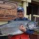 A man hugging big Chinook salmon in front of King Pacific Lodge